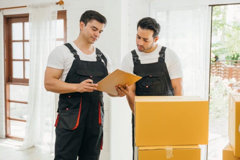 Professional movers holding a box while checking their clipboard in the concept of man and van in East London.