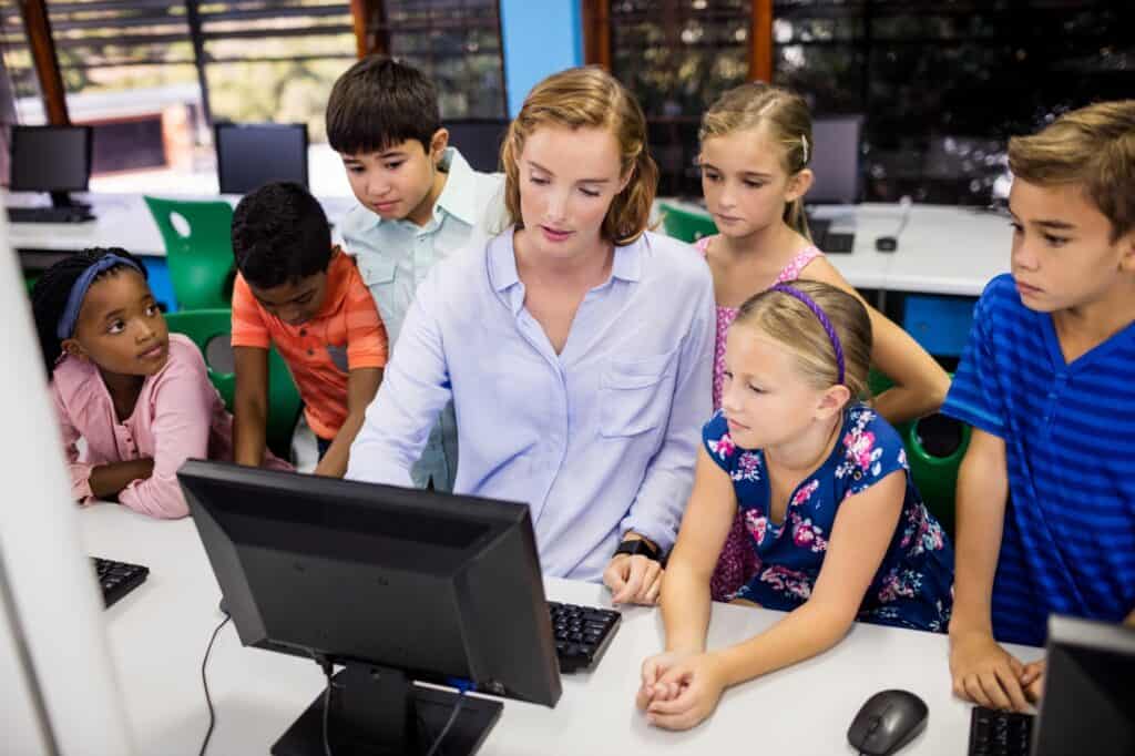 A teacher is giving a lesson to her students with a computer in the concept of schools in East London.